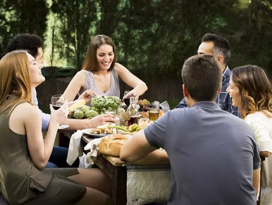 Grupo de personas charlando mientras ríen y disfrutan de una comida al aire libre